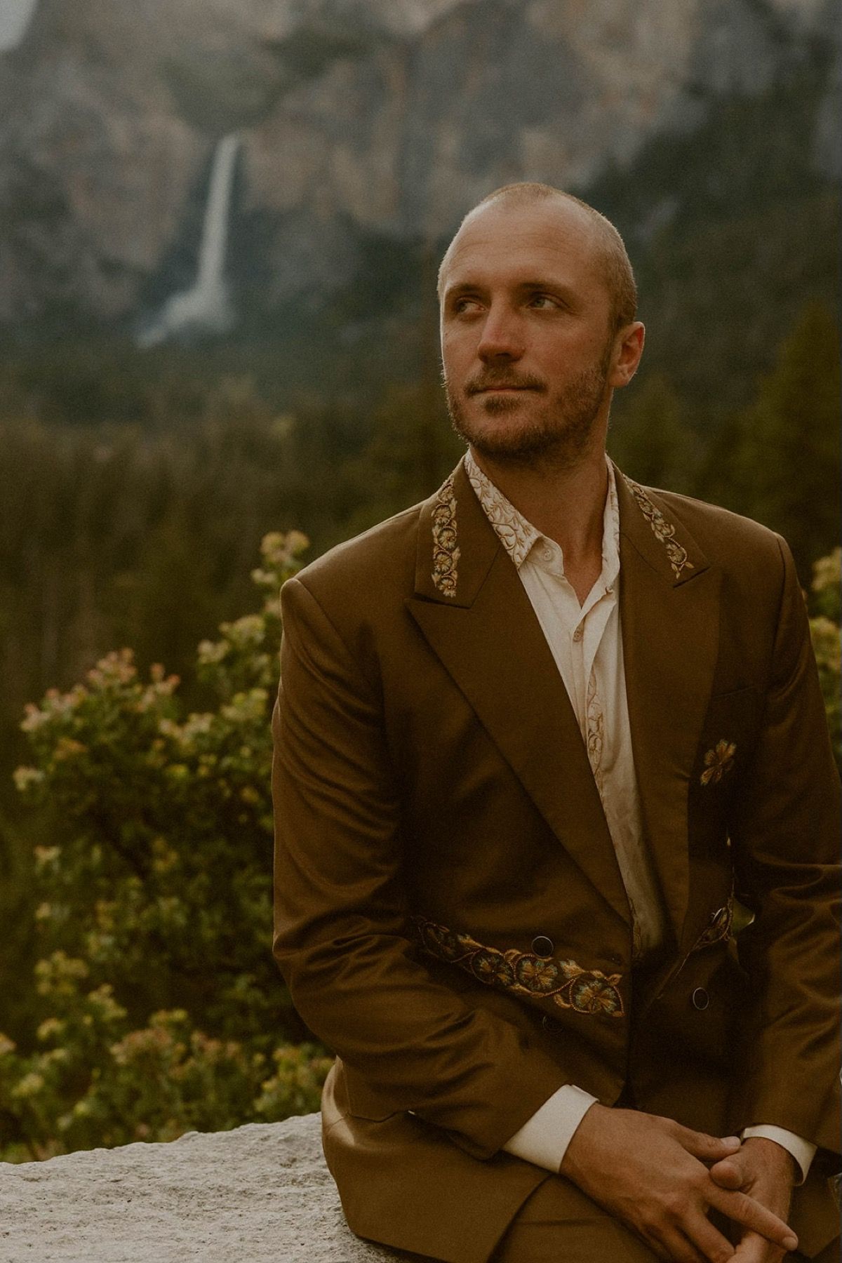 A groom in a brown double-breasted suit with embroidered lapels, seated in Yosemite Valley